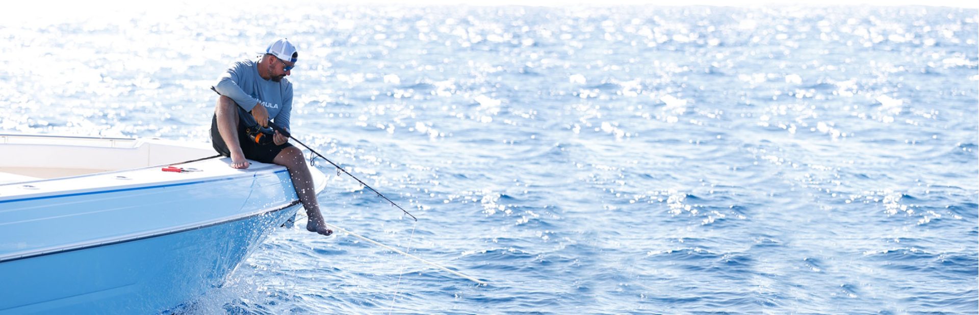 a man sits on the side of a boat fishing
